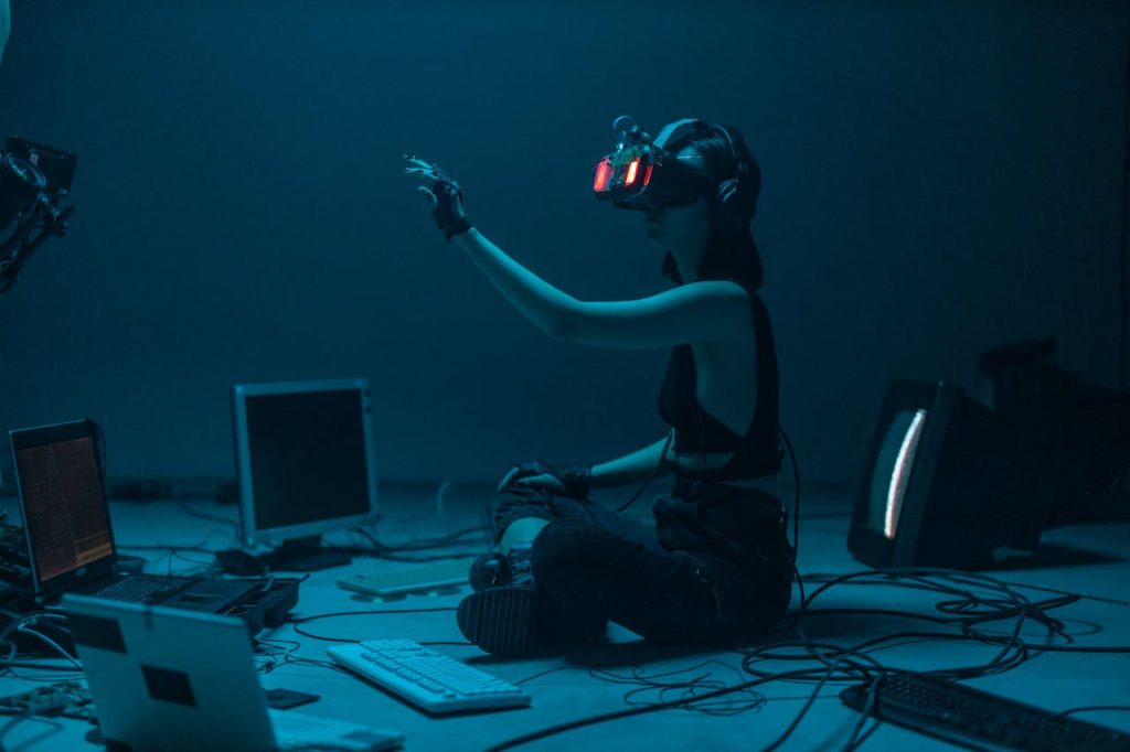 pexels-photo-8721318 Woman immersed in virtual reality, surrounded by tech, in a dimly lit room.